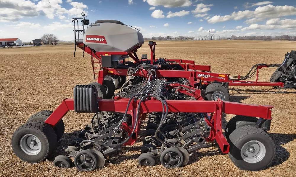 A red Case IH seed planter in a field, showcasing modern agricultural machinery used for large-scale crop production under a clear sky with scattered clouds.