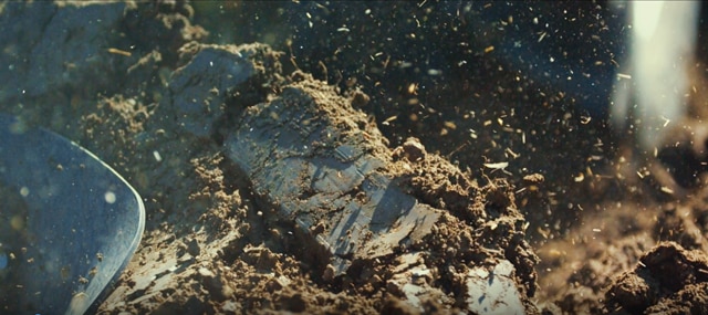 Close-up action shot of soil being dug, with particles and clumps of earth in mid-air, highlighting the dynamic motion and texture of the soil.